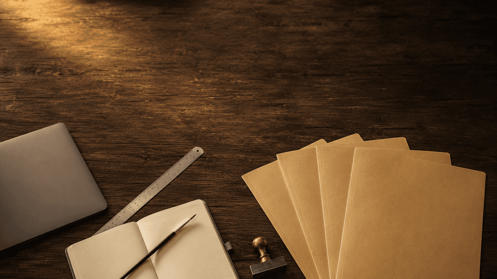 A worn wooden desk photographed from above under warm amber light, holding the tools of self-employment — a laptop, an architect's ruler, a paintbrush, a notary's stamp, and a stack of unlabeled residence-permit folders fanned out like a hand of cards. No country flags, no readable text. The image represents the central idea of the article: the same self-employed person carries the same tools across every border, but each country asks a completely different question about whether those tools qualify them to stay.